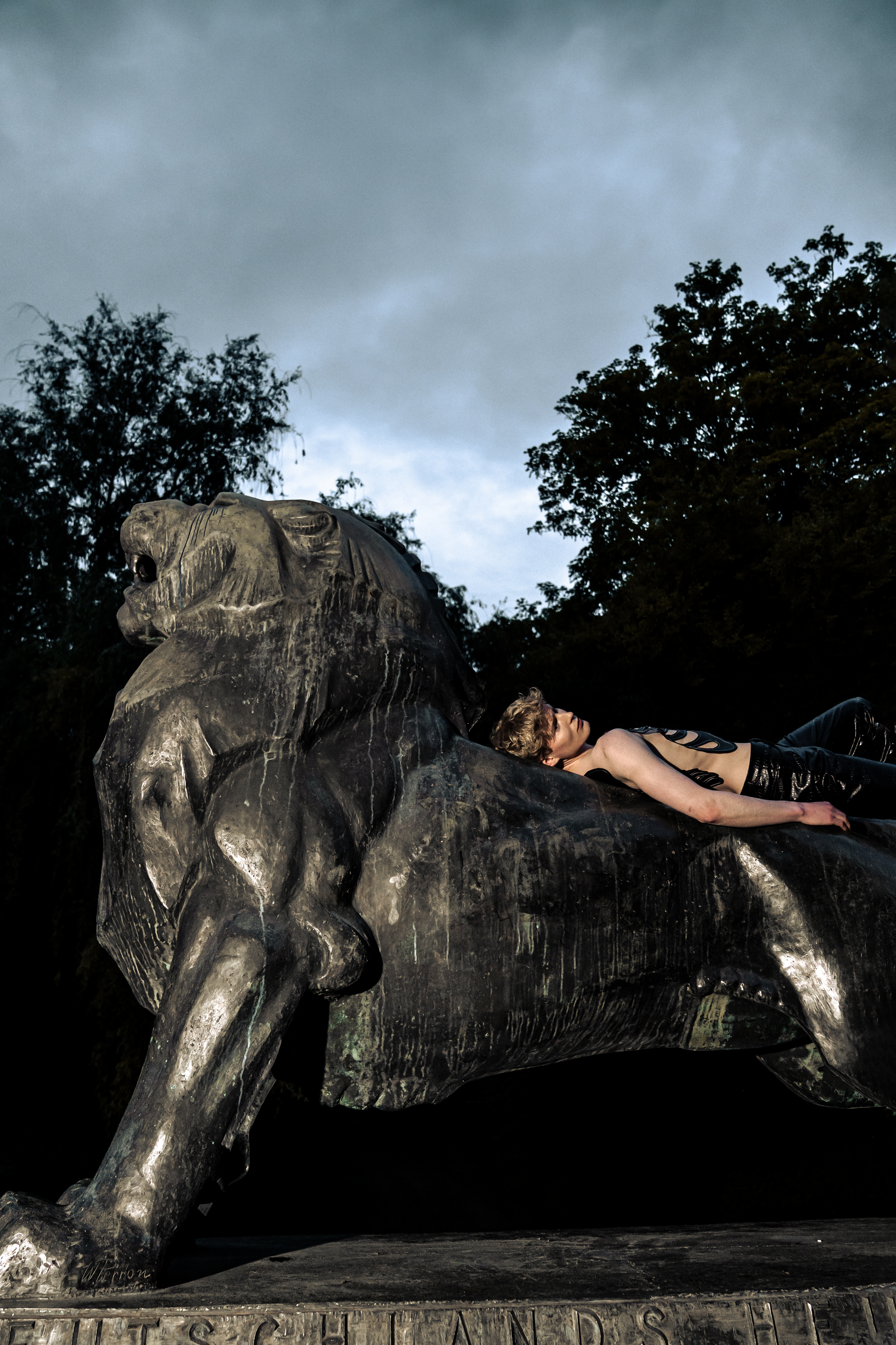 Model wearing a black skeleton cuirass and snakeskin leather trousers lying on the lion statue.