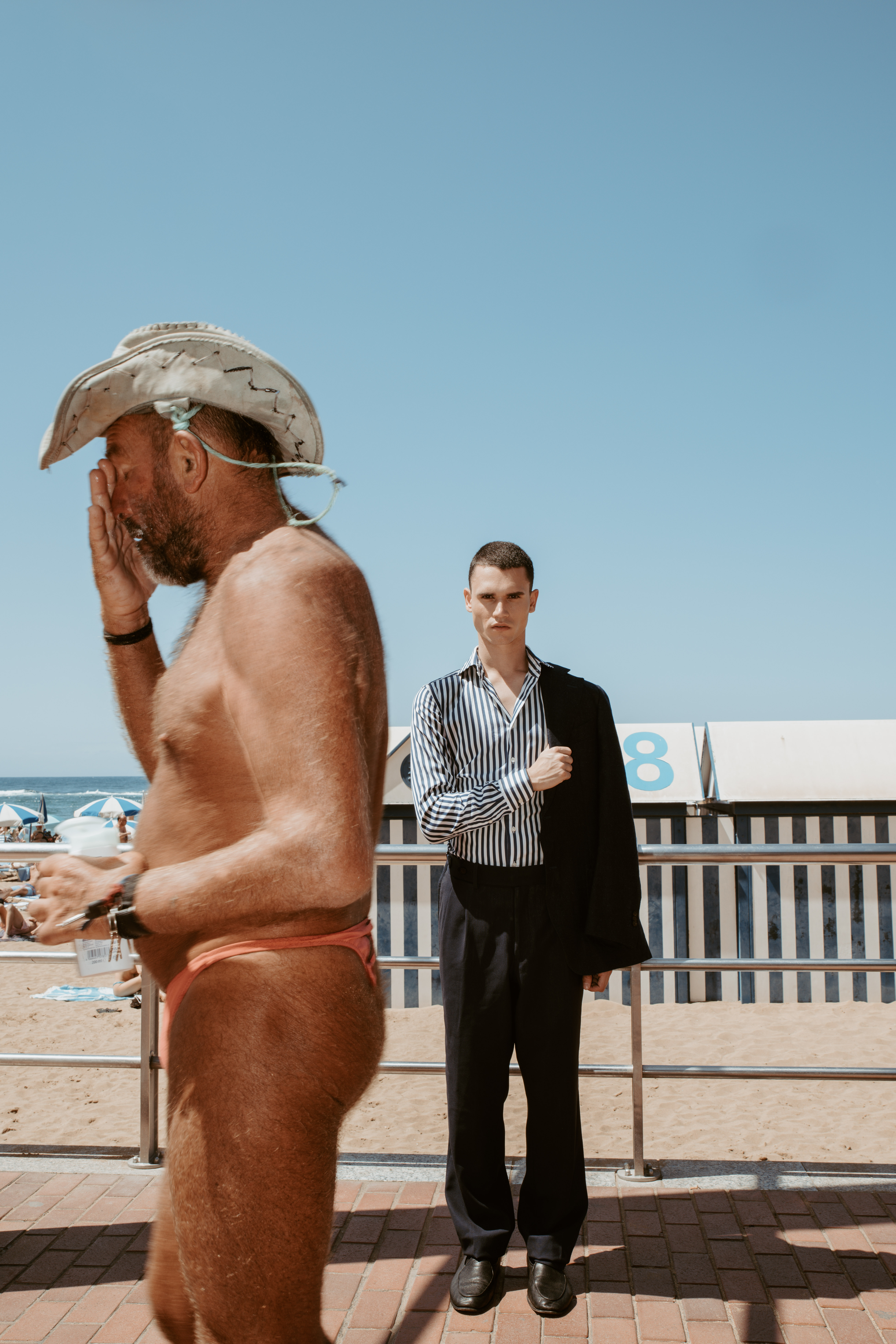 Modelo con traje de sastrería en un entorno de playa rodeada de bañistas en un editorial de moda