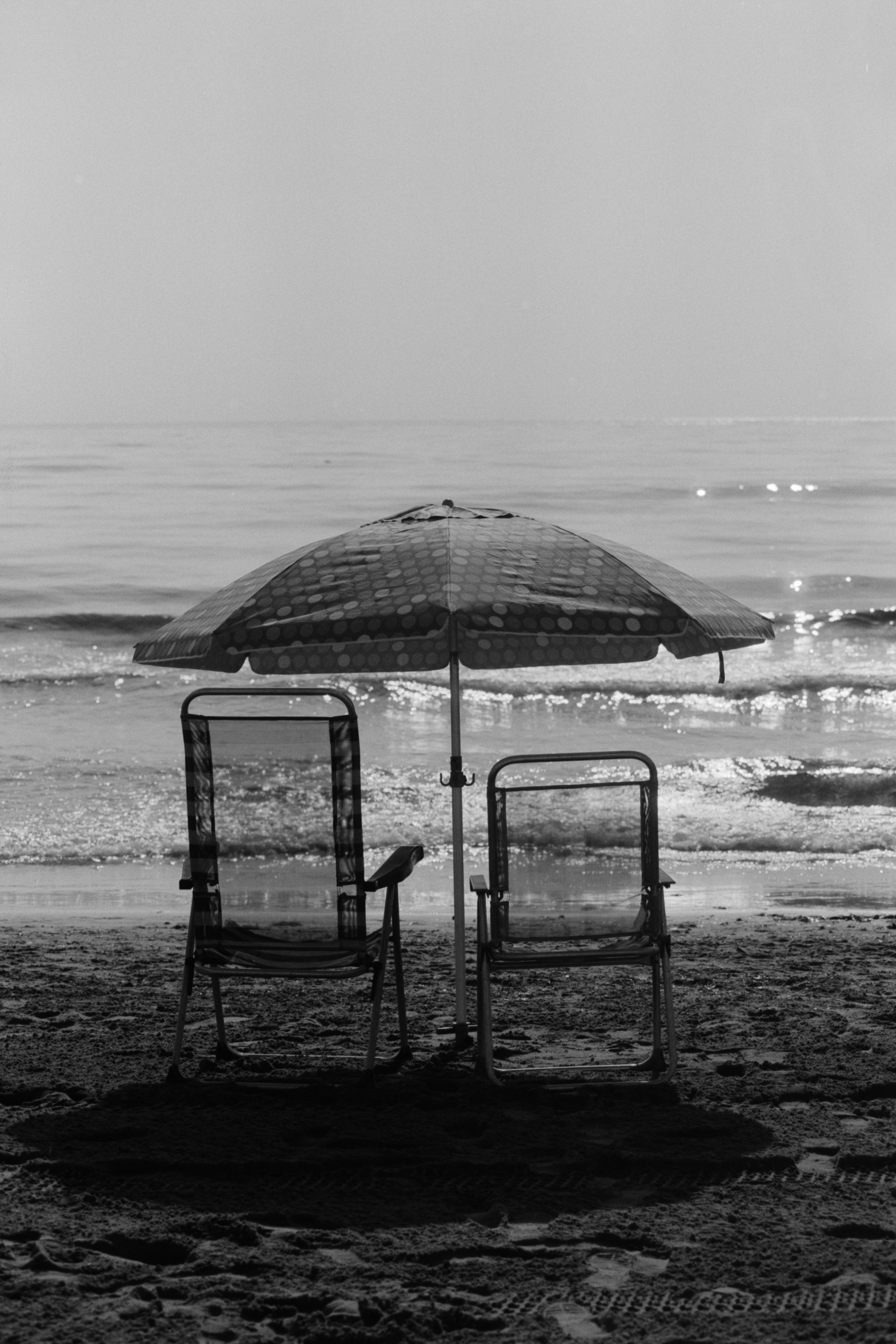 Sillas vacías y sombrilla frente al mar en Alicante en una escena en blanco y negro