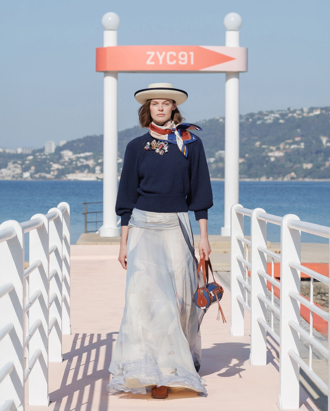 Modelo con sudadera azul marino, falda maxi con estampado de velas y sombrero Panamá de la colección The Clash de ZIMMERMANN Cruise RTW 2027