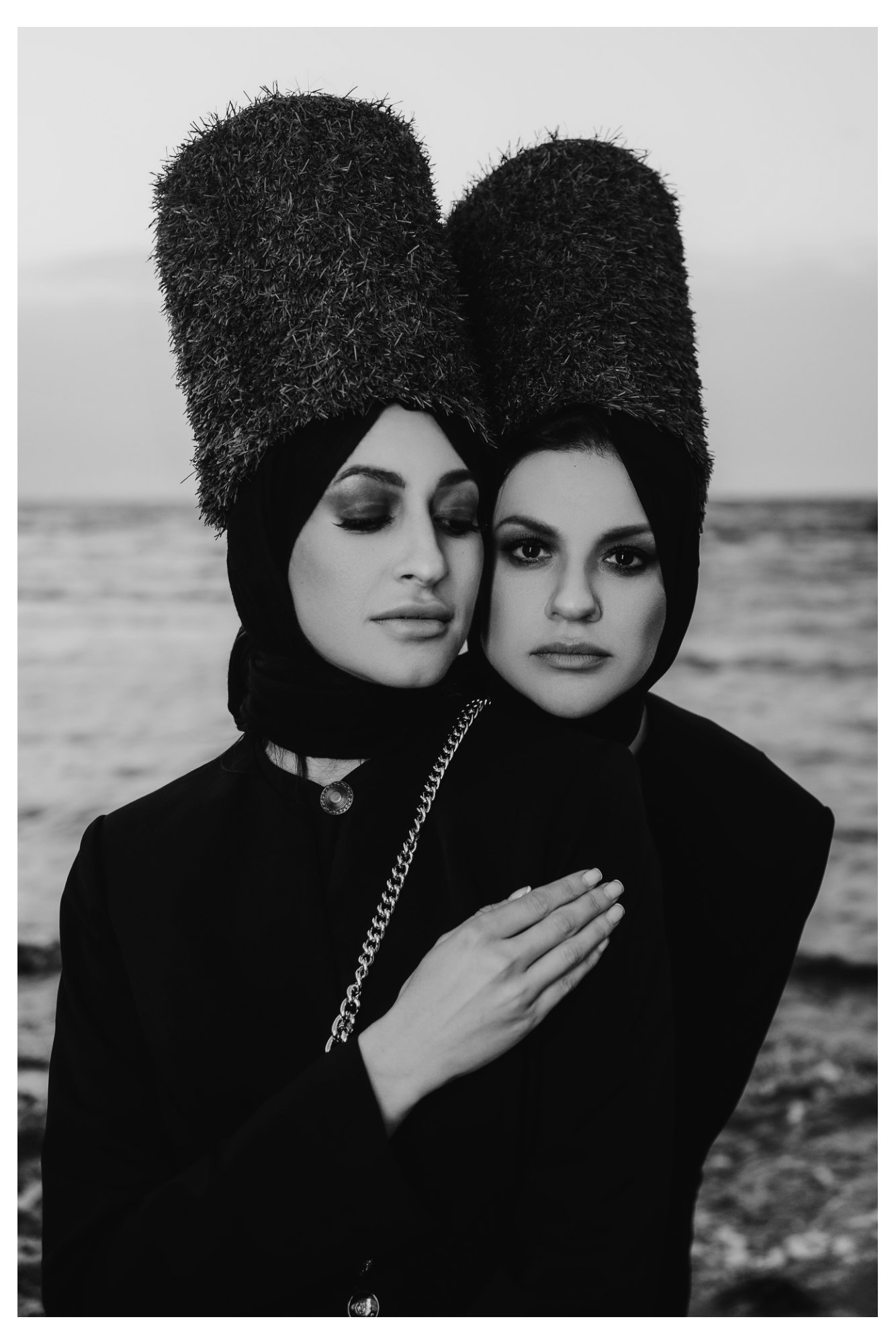 Two women shown in close-up wearing dramatic structured crinolines and towering hats in a fashion editorial