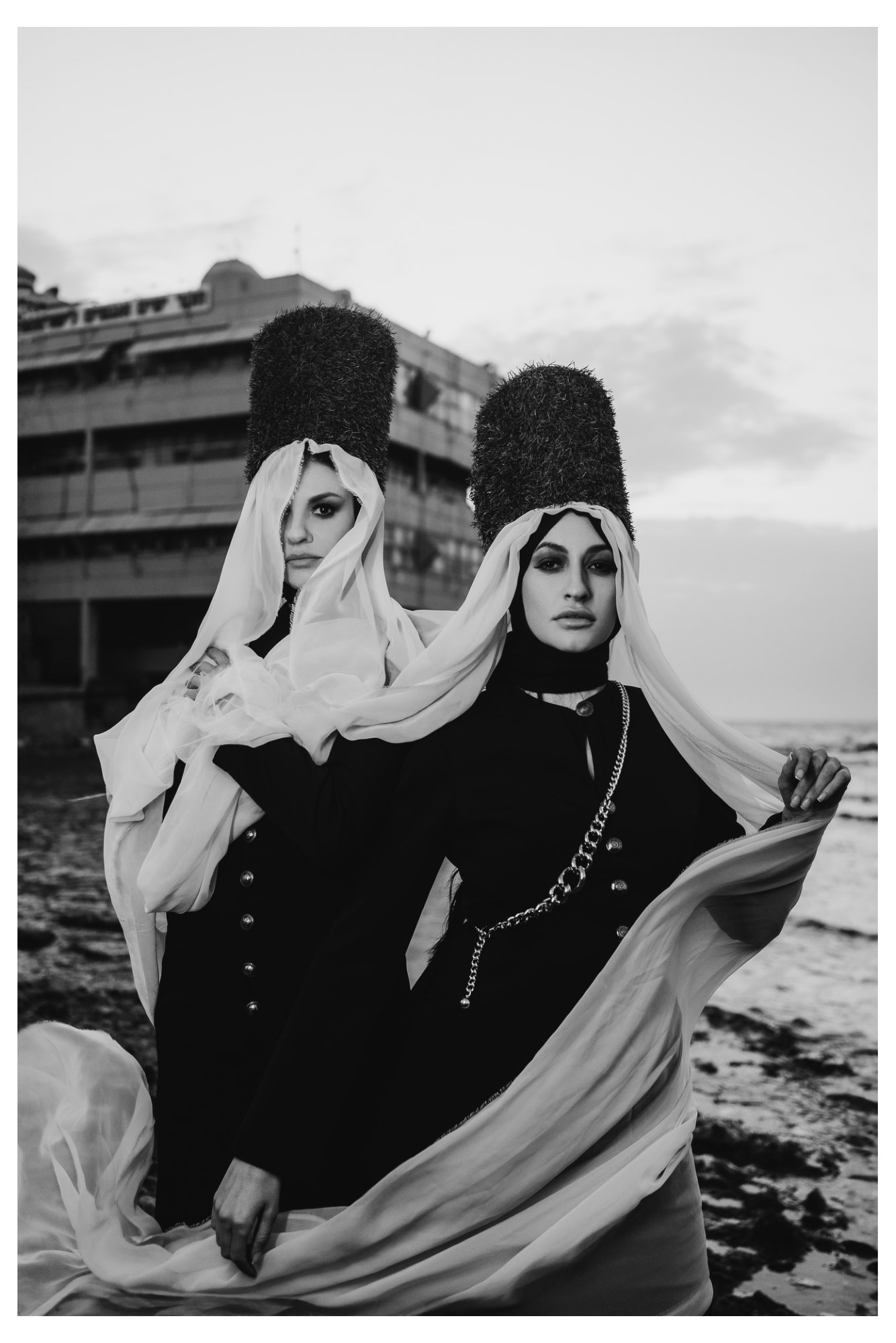 Two women wearing flowing scarves in a black-and-white fashion editorial, with confident poses and shared gestures